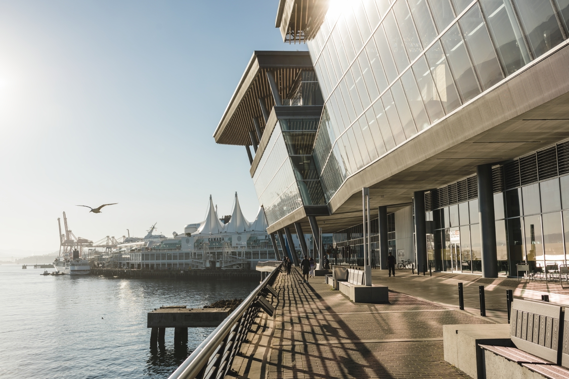 Outside of the Vancouver Convention Centre on a sunny day. This glass building sits on the waters edge in downtown Vancouver and has a concrete walkway around it.