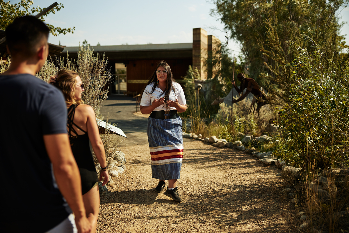 A woman faces the camera, talking to a tour group and leading a cultural tour. A couple watches and listens.